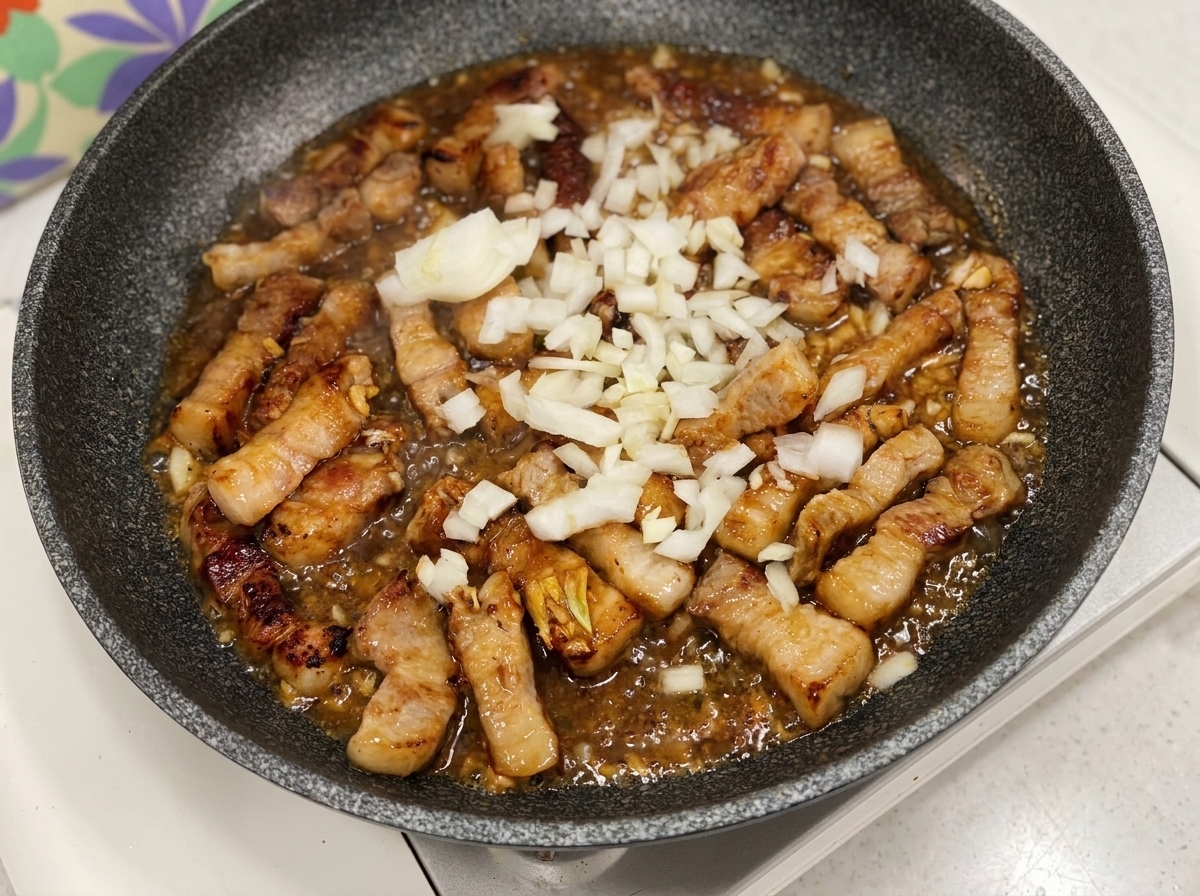 Gehackte weiße Zwiebeln werden in die Pfanne mit Fleisch und blubbernder dunkler Sauce gegeben.