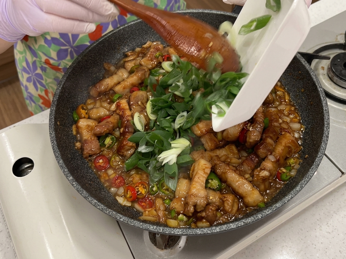 Grüne und rote Chilis sowie Frühlingszwiebeln werden in die Pfanne gestreut.
