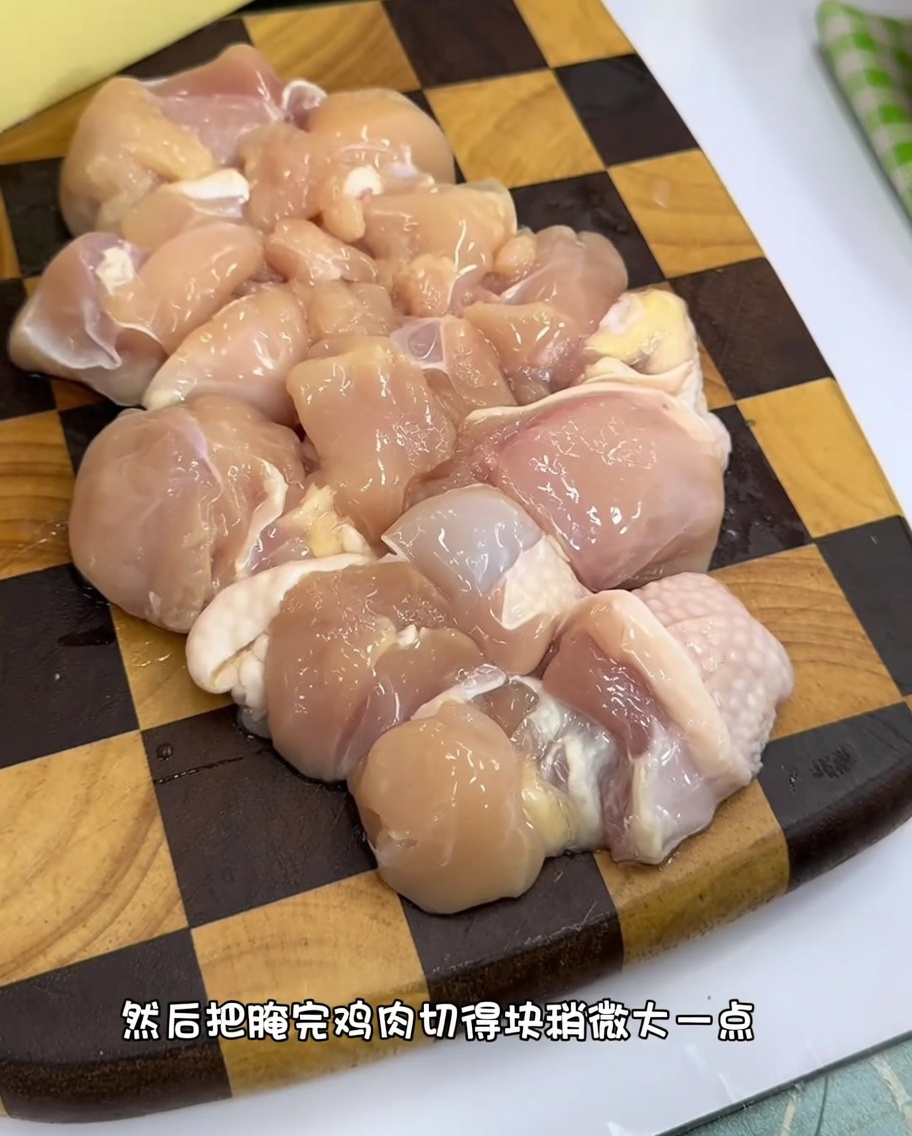 Gleichmäßige Stücke rohes Hähnchenfleisch auf einem Holzbrett.