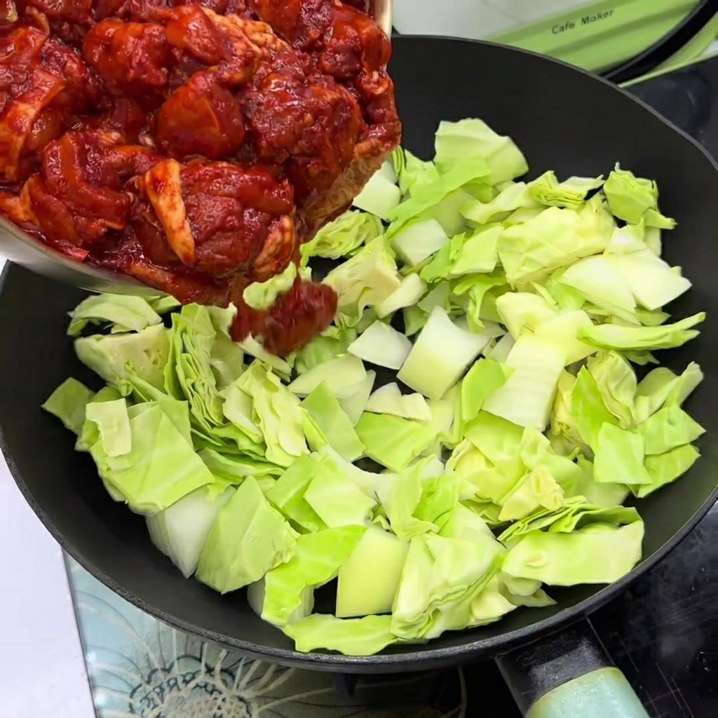 Mariniertes Hähnchen auf Kohl und Zwiebeln in einer Pfanne.
