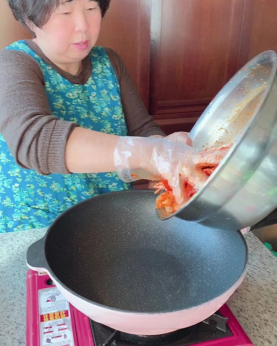 Die marinierte Mischung aus Schweinebauch, Tintenfisch und Gemüse wird aus einer Edelstahlschüssel in eine heiße Pfanne gegeben.