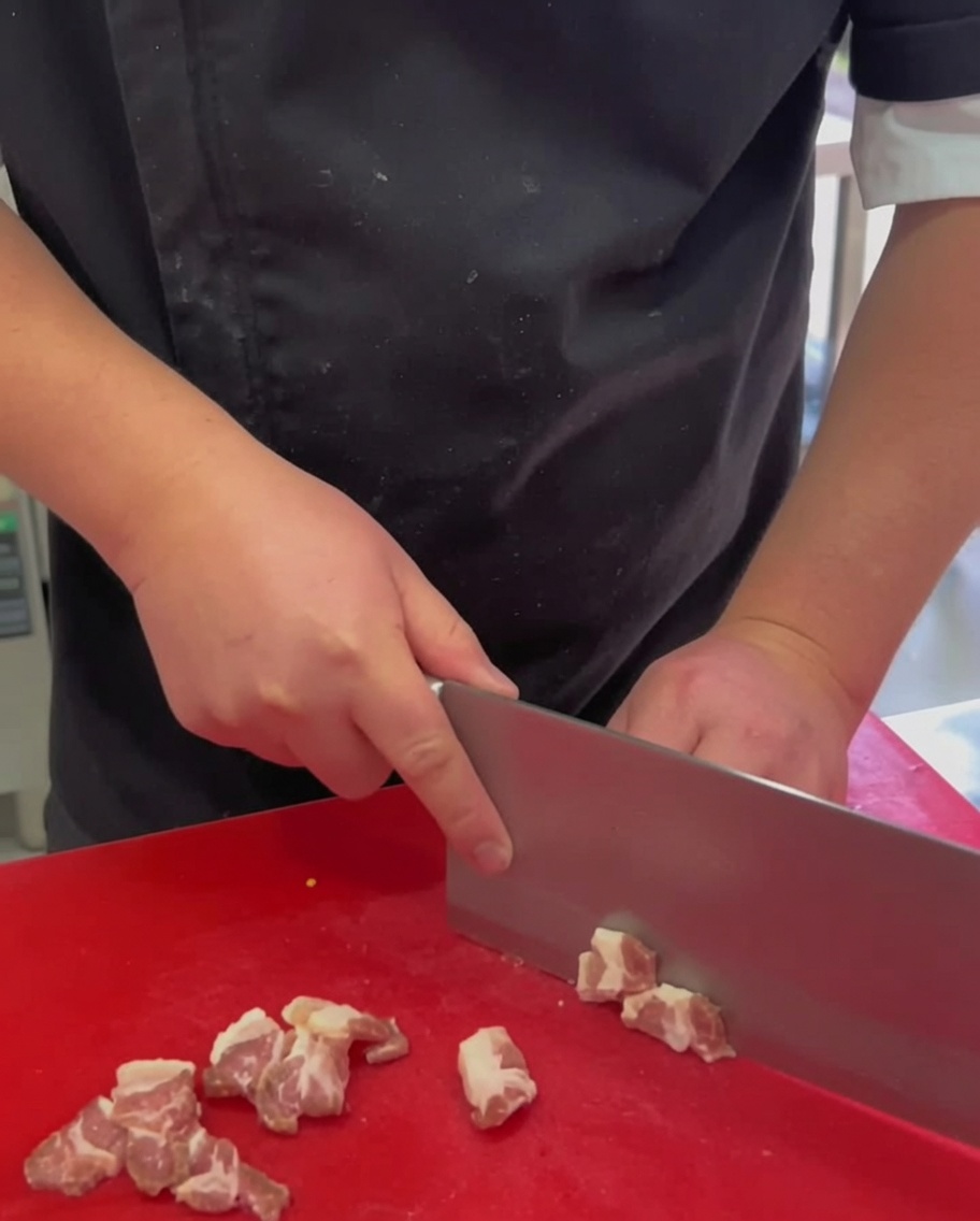 Dünne Scheiben roher Schweinebauch auf einem roten Schneidebrett.