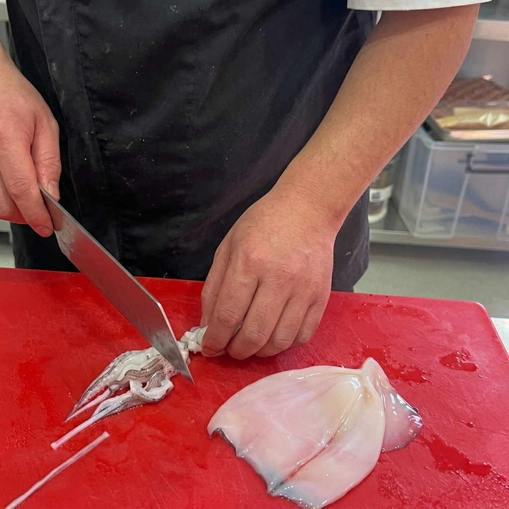 Geputzter Tintenfisch, der auf einem roten Schneidebrett in Ringe geschnitten wird.