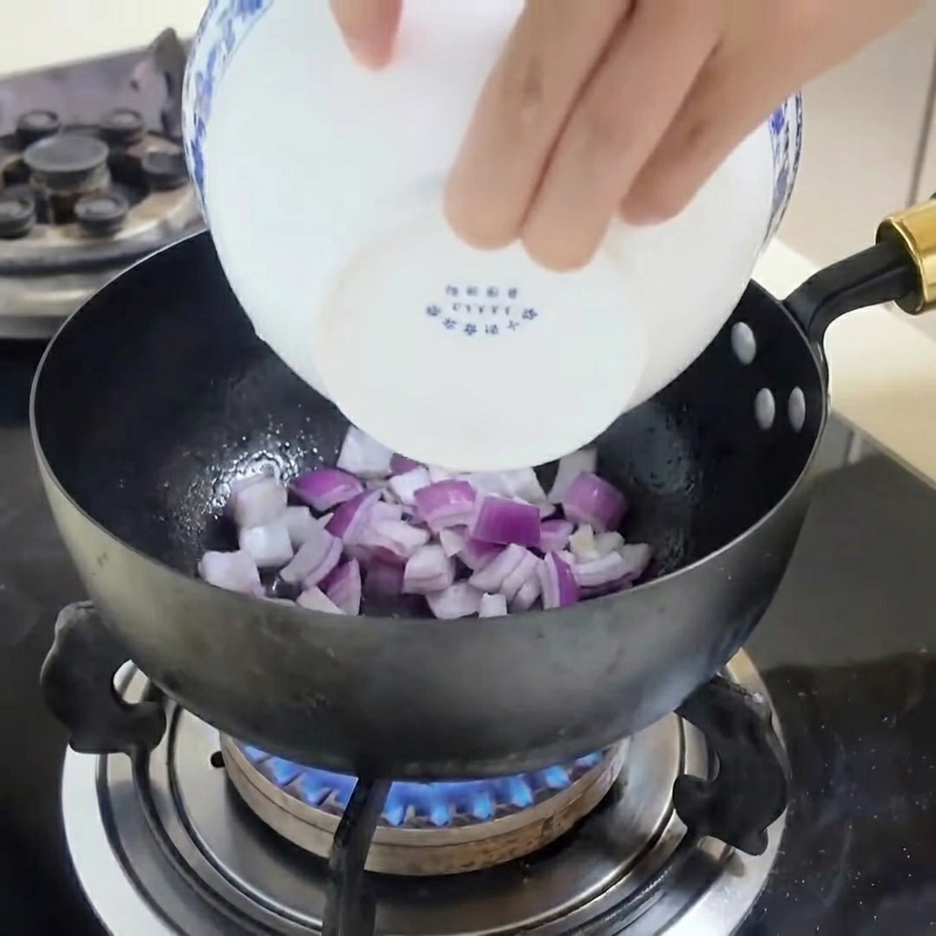 Angebratene rote Zwiebelstreifen in einer Pfanne mit Kochspray.