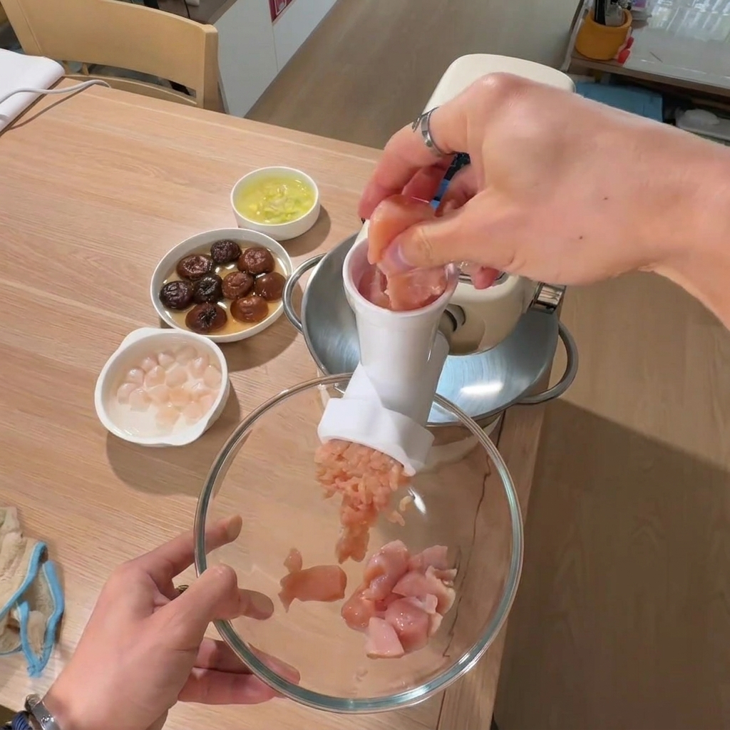 Eine Hand legt Hähnchenbruststücke in eine große Schüssel, mit Schalen von eingeweichten Pilzen und Jakobsmuscheln im Hintergrund.