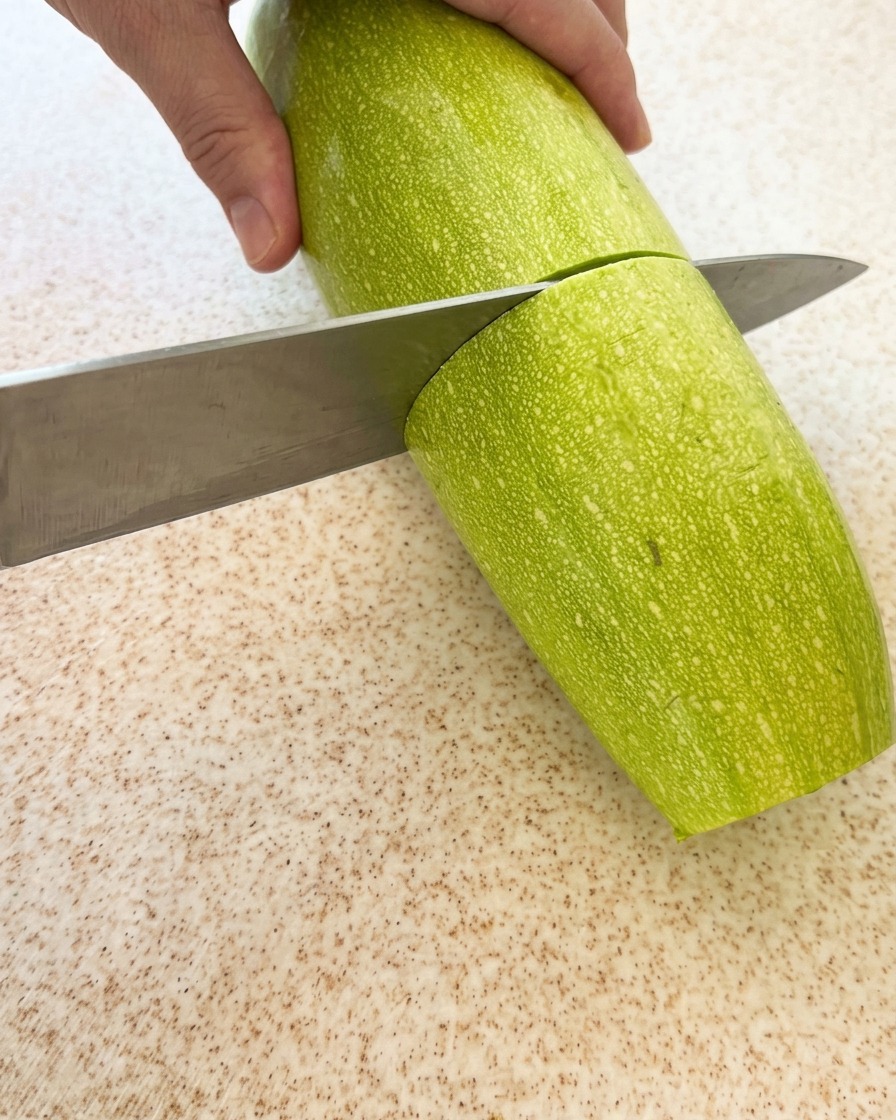 Eine frische grüne Zucchini wird auf einem Schneidebrett in Stücke geschnitten.