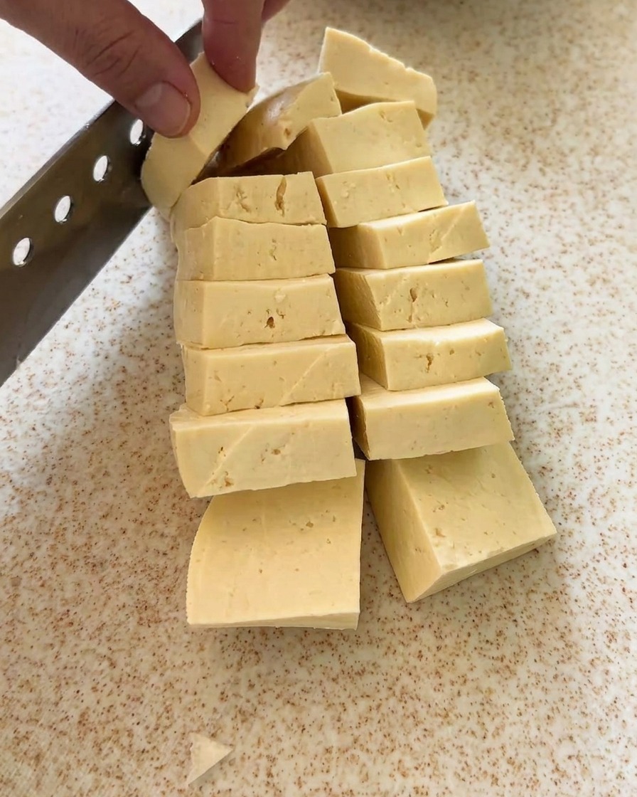 Ein Tofublock wird in saubere, gleichmäßige Würfel geschnitten.