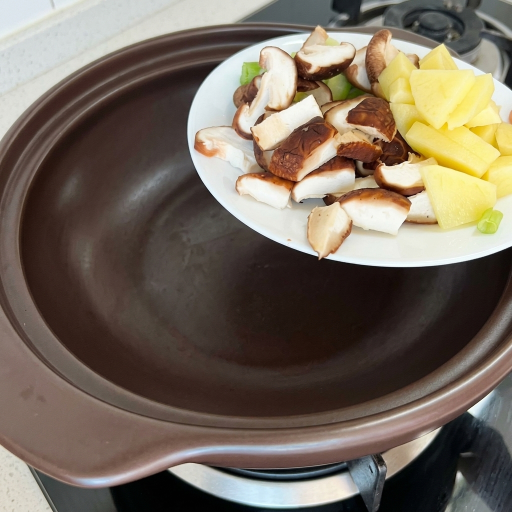 Gehackte Kartoffeln, Zucchini und Shiitake-Pilze werden in einen braunen Tontopf gegeben.