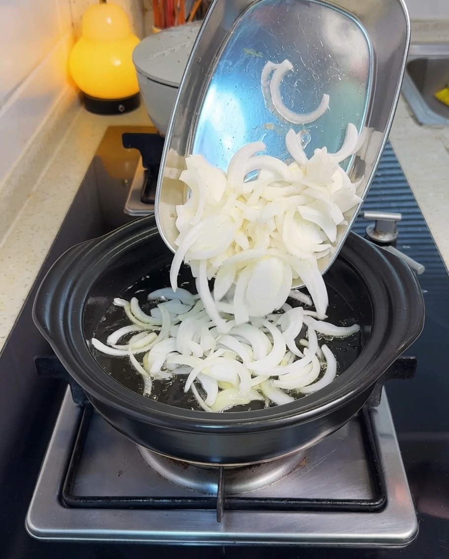 In Scheiben geschnittene Zwiebeln werden in einem heißen Topf mit Öl angebraten.