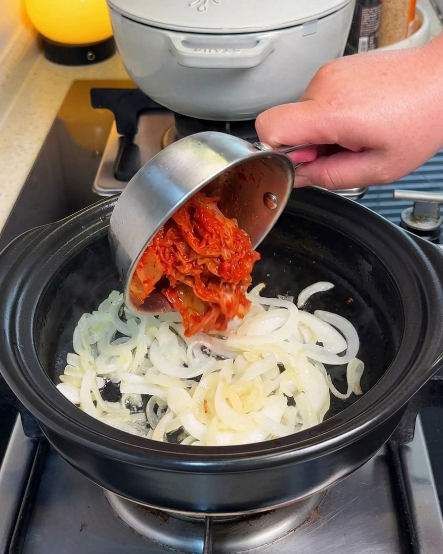 Kimchi wird zu den angebratenen Zwiebeln in den Topf gegeben.
