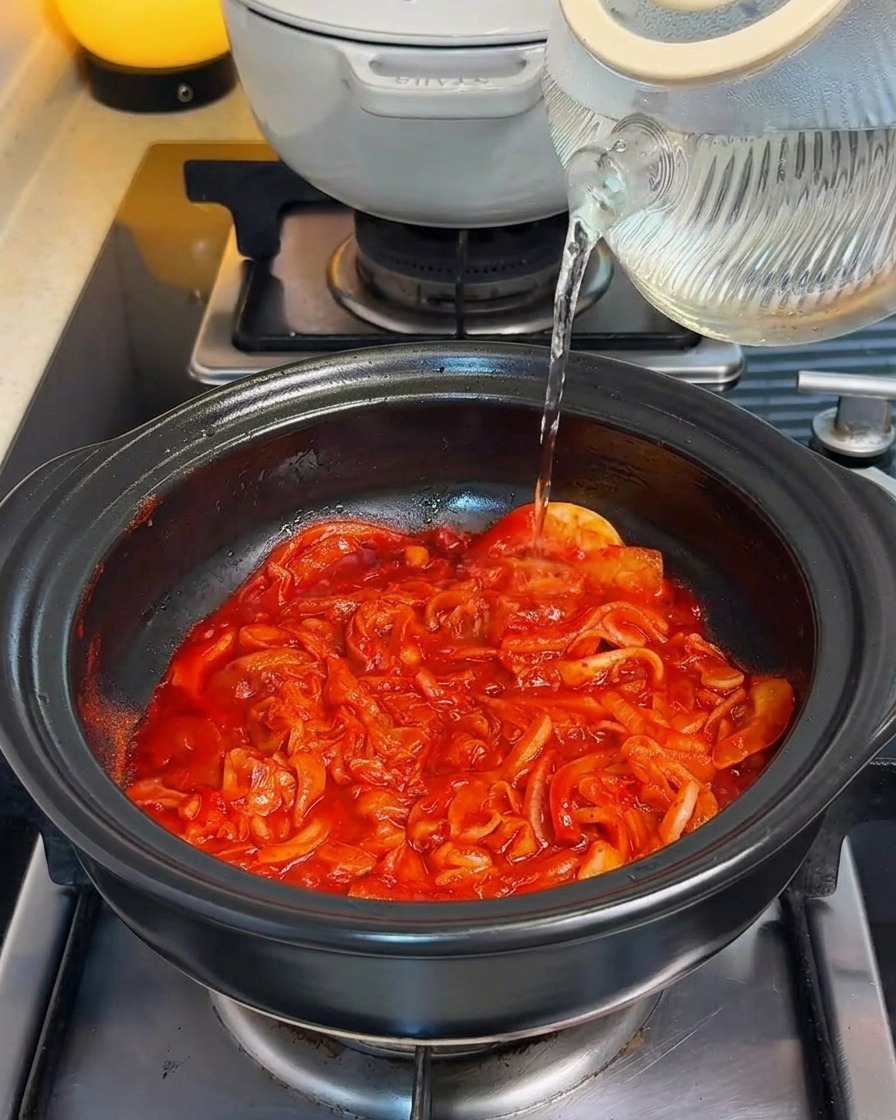 Frisches Wasser wird in einen Topf mit der leuchtend roten Kimchi-Basis gegossen.