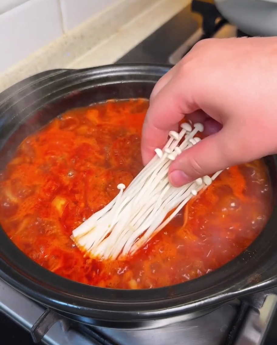 Enoki-Pilze und Seidentofuwürfel werden vorsichtig in die köchelnde Kimchi-Suppe gegeben.