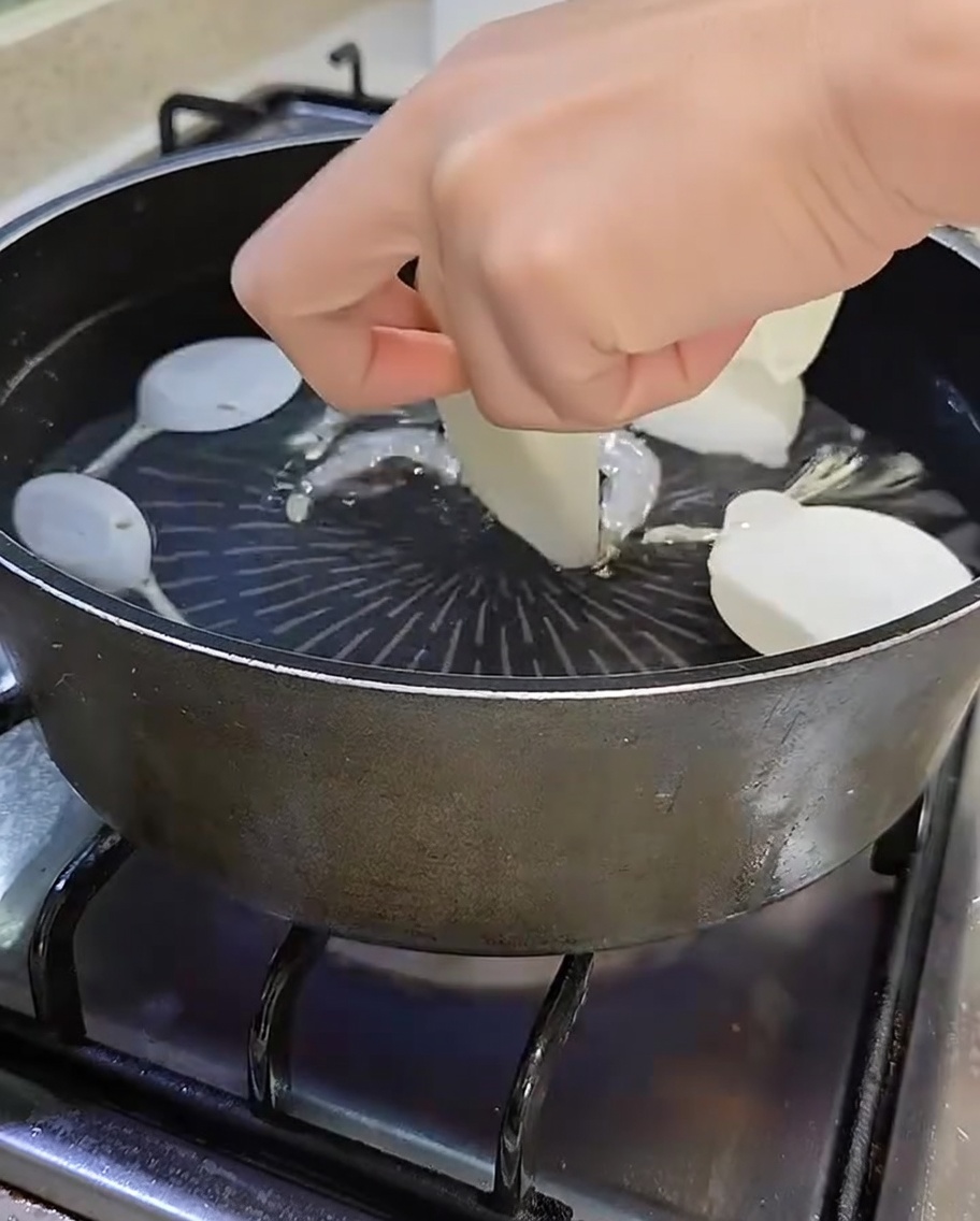 Topf mit kochendem Wasser, Sardellen, Shiitake, in Scheiben geschnittenem Rettich und grünen Frühlingszwiebeln.