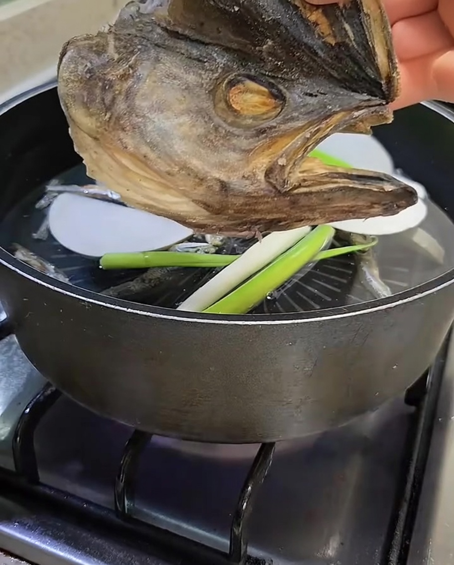 Ein getrockneter Pollack-Fischkopf wird über den Topf gehalten, bevor er in die Brühe gegeben wird.