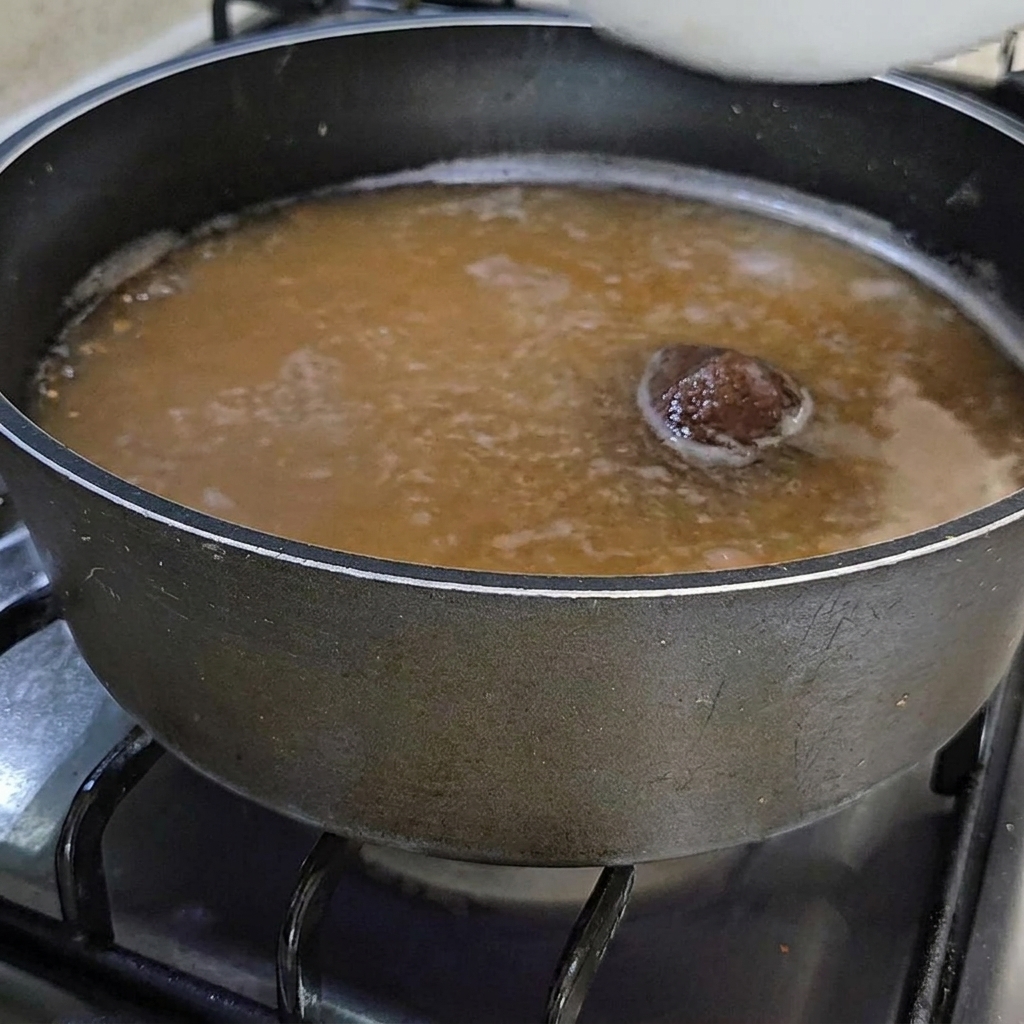 Eine Schüssel mit frischen, orangefarbenen Seescheiden wird in die köchelnde Sojabohnenpastenbrühe gegeben.