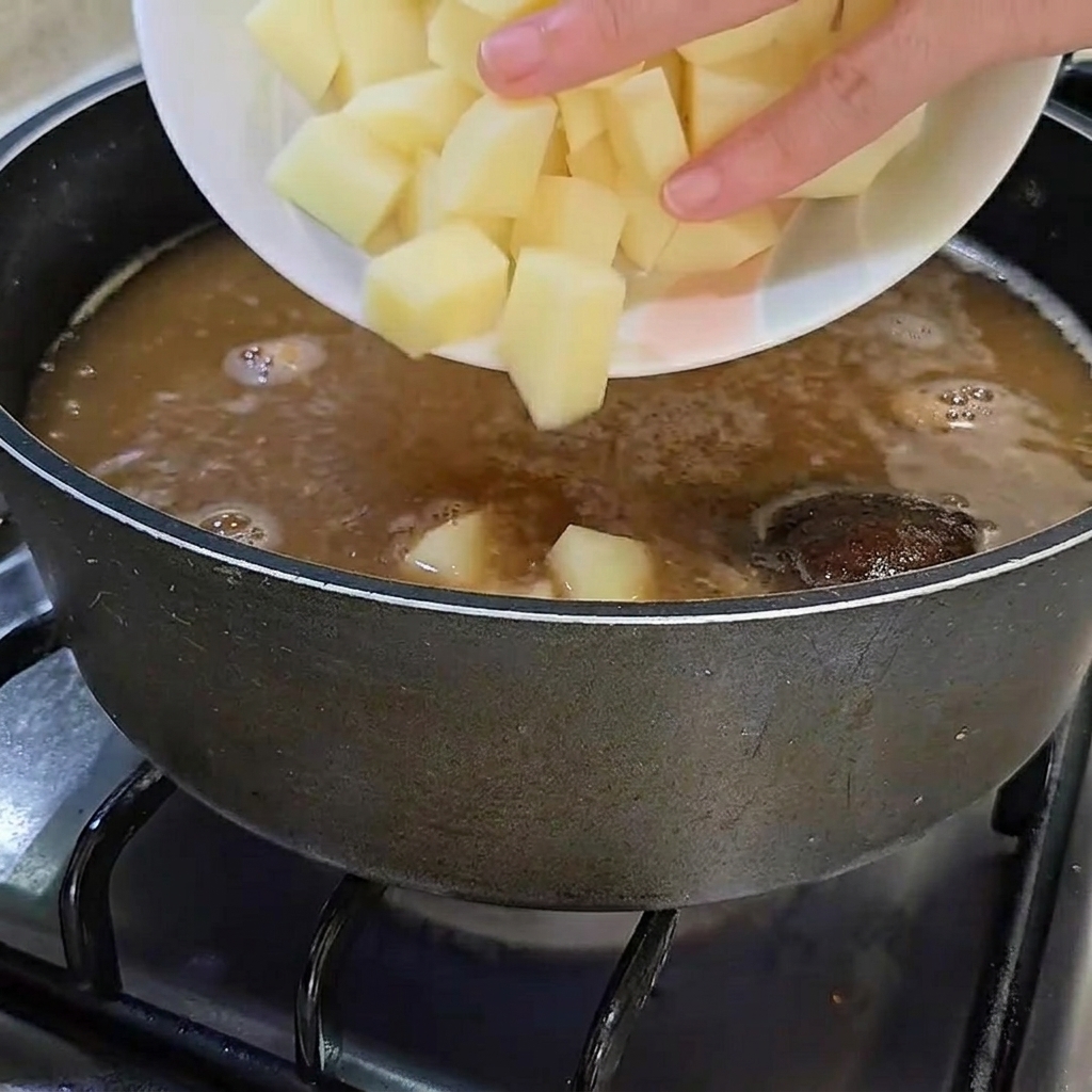 Frisch gewürfelte rohe Kartoffeln werden in den Topf mit der köchelnden Brühe gegeben.