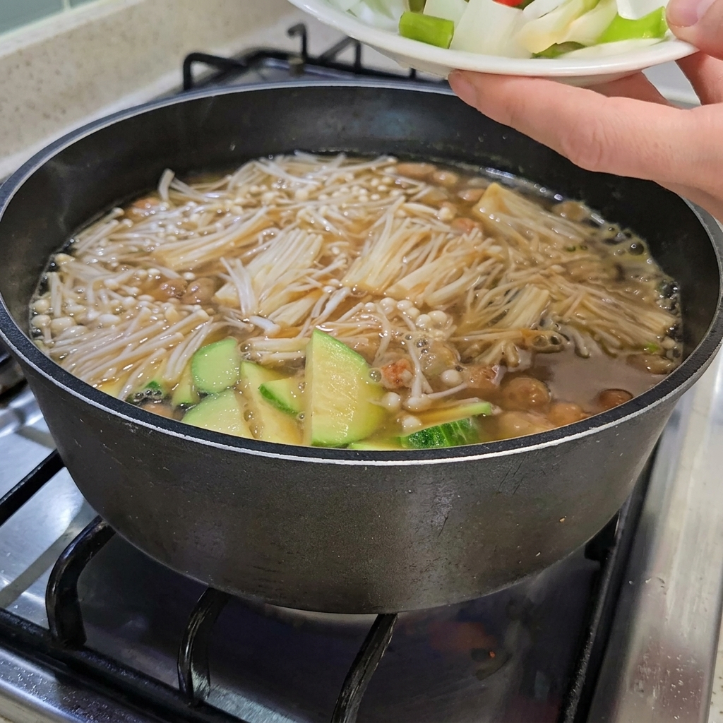 Gehackte Zwiebeln, Frühlingszwiebeln sowie rote und grüne Chilischoten werden zum Eintopf hinzugefügt, der auch geschnittenen Tofu enthält.