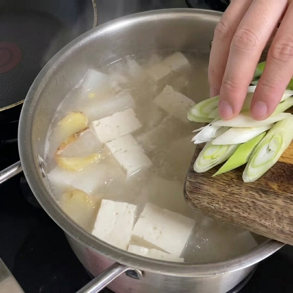 Frisch gehackte Frühlingszwiebeln werden über die kochende Pollack-Suppe gestreut.