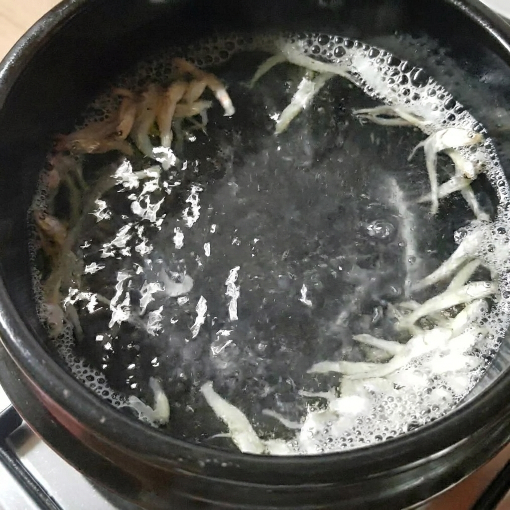 Ein schwarzer Steintopf mit Wasser, getrockneten Sardellen und Seetang auf dem Herd.