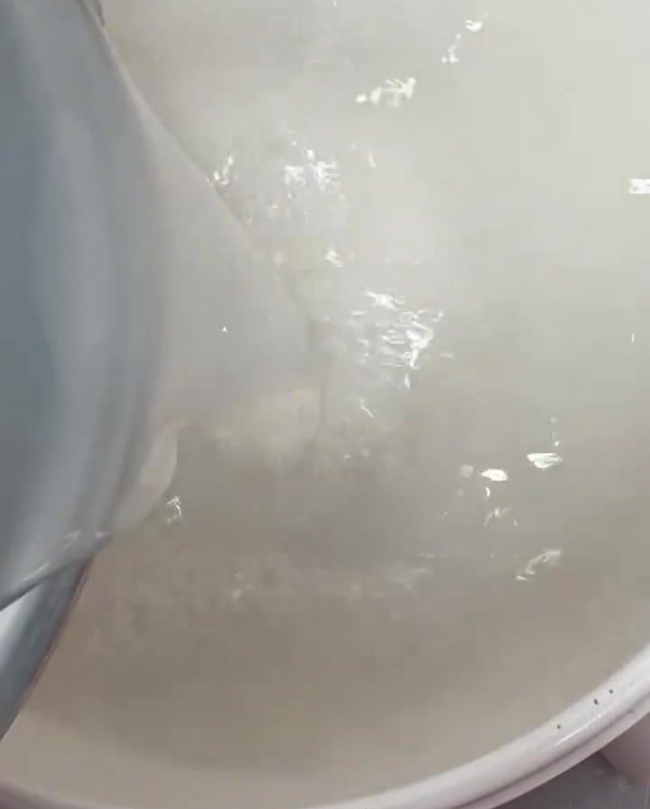 Klares, weißes Reiswasser wird in einen großen Kochtopf gegossen.