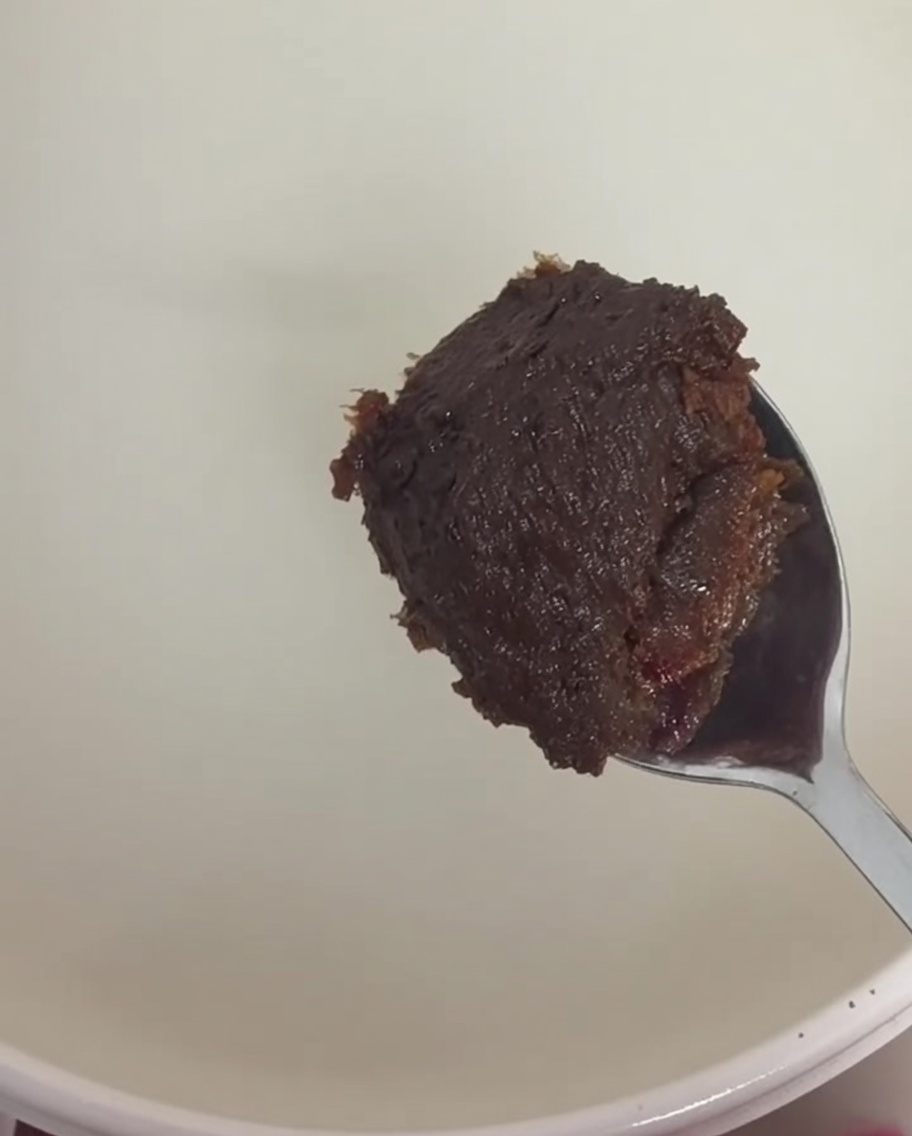 Ein Löffel dicker brauner Sojapaste und dunkelroter Chilipaste werden in die Reiswasserbrühe gerührt.