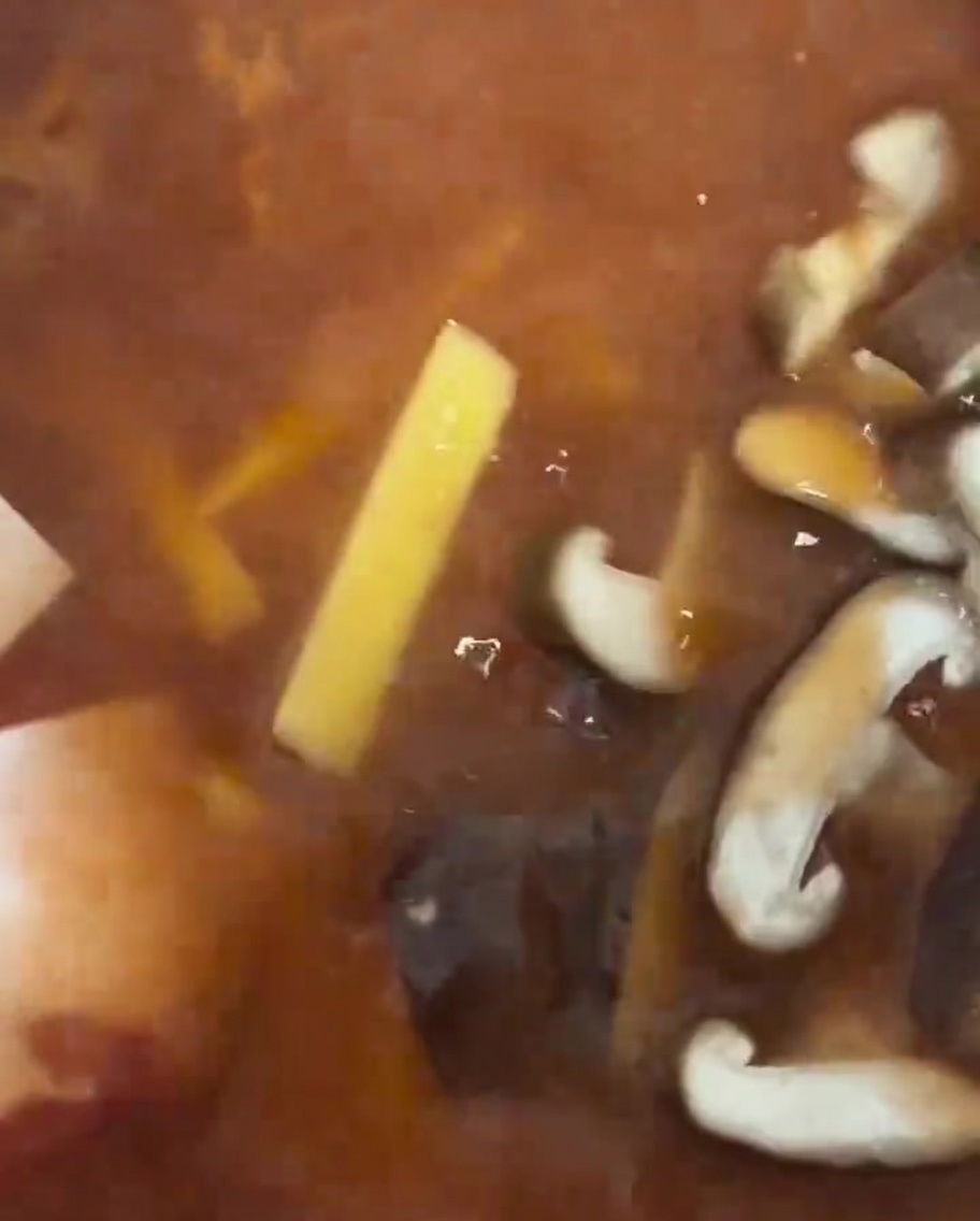 Scheiben von frischen Shiitake-Pilzen werden in den Eintopf gelegt.