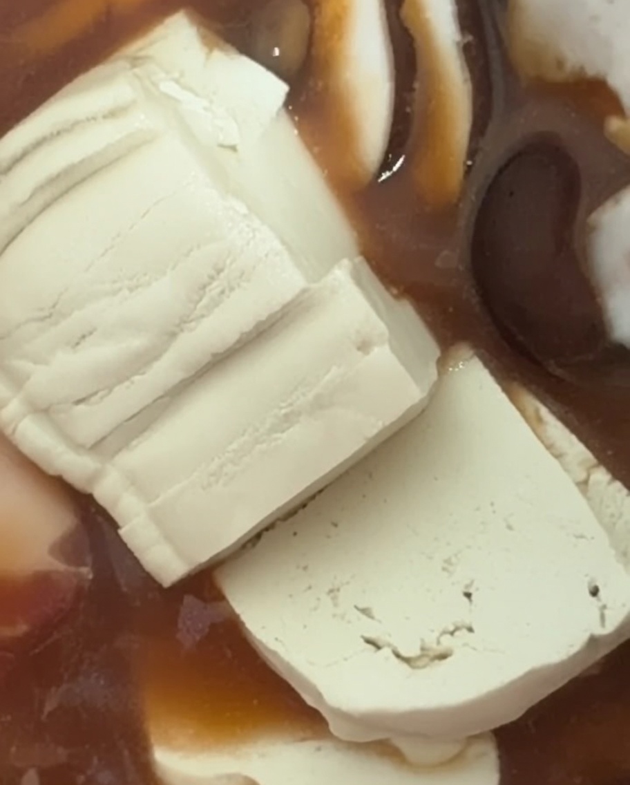 Frische, weiche weiße Tofuscheiben werden in den blubbernden Eintopf geschichtet.