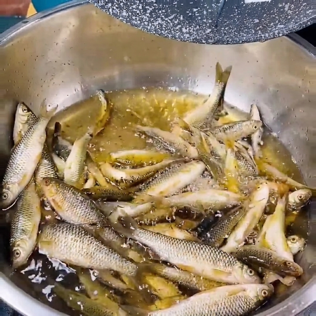 Kleiner frischer Flussfisch, der in einer Metallschüssel mit klarem Wasser abgespült wird.