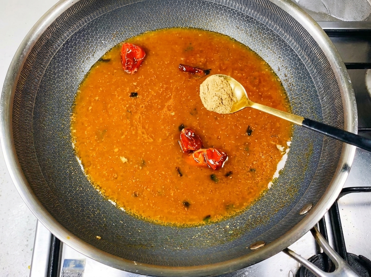 Gewürzpulver wird in die köchelnde, orangefarbene Brühe im Wok gestreut.