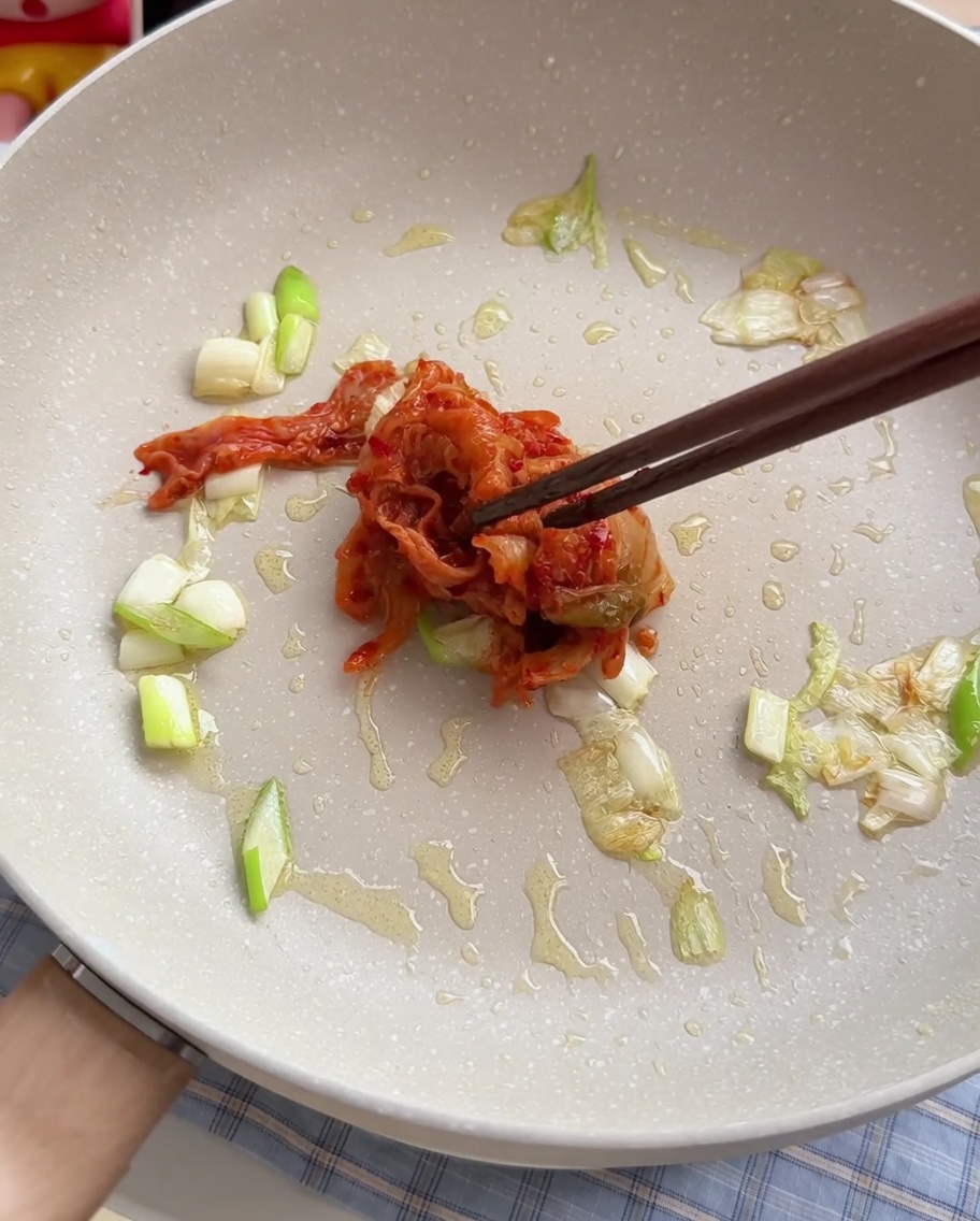 Kimchi wird in einer Pfanne mit angeschwitzten Frühlingszwiebeln umgerührt.