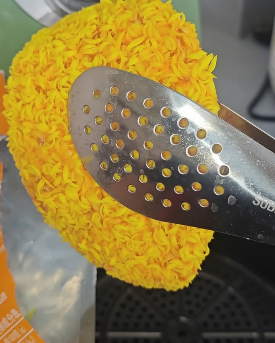 Gefrorene Hähnchenfilets werden mit einer Metallzange in den Korb der Heißluftfritteuse gelegt.