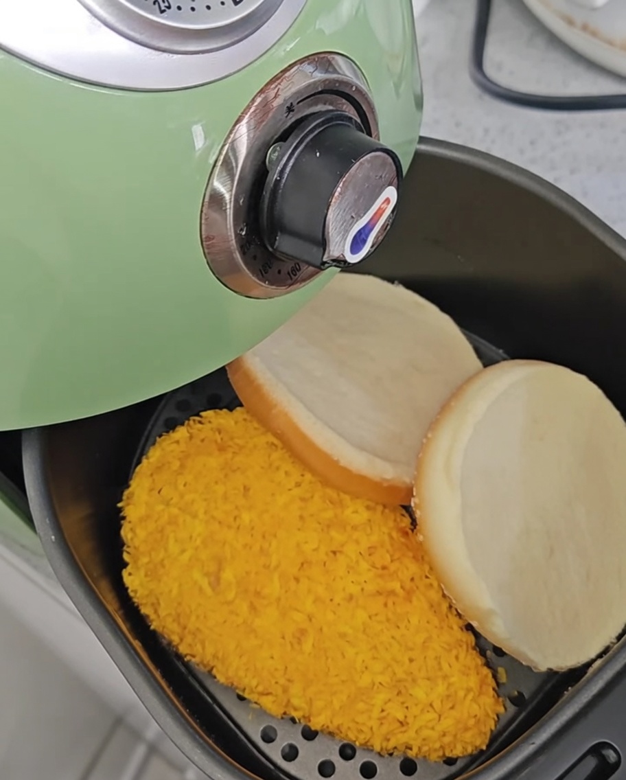 Hähnchenfilets in der Heißluftfritteuse, nachdem sie gewendet wurden, mit zwei daneben liegenden Burger-Brötchen.