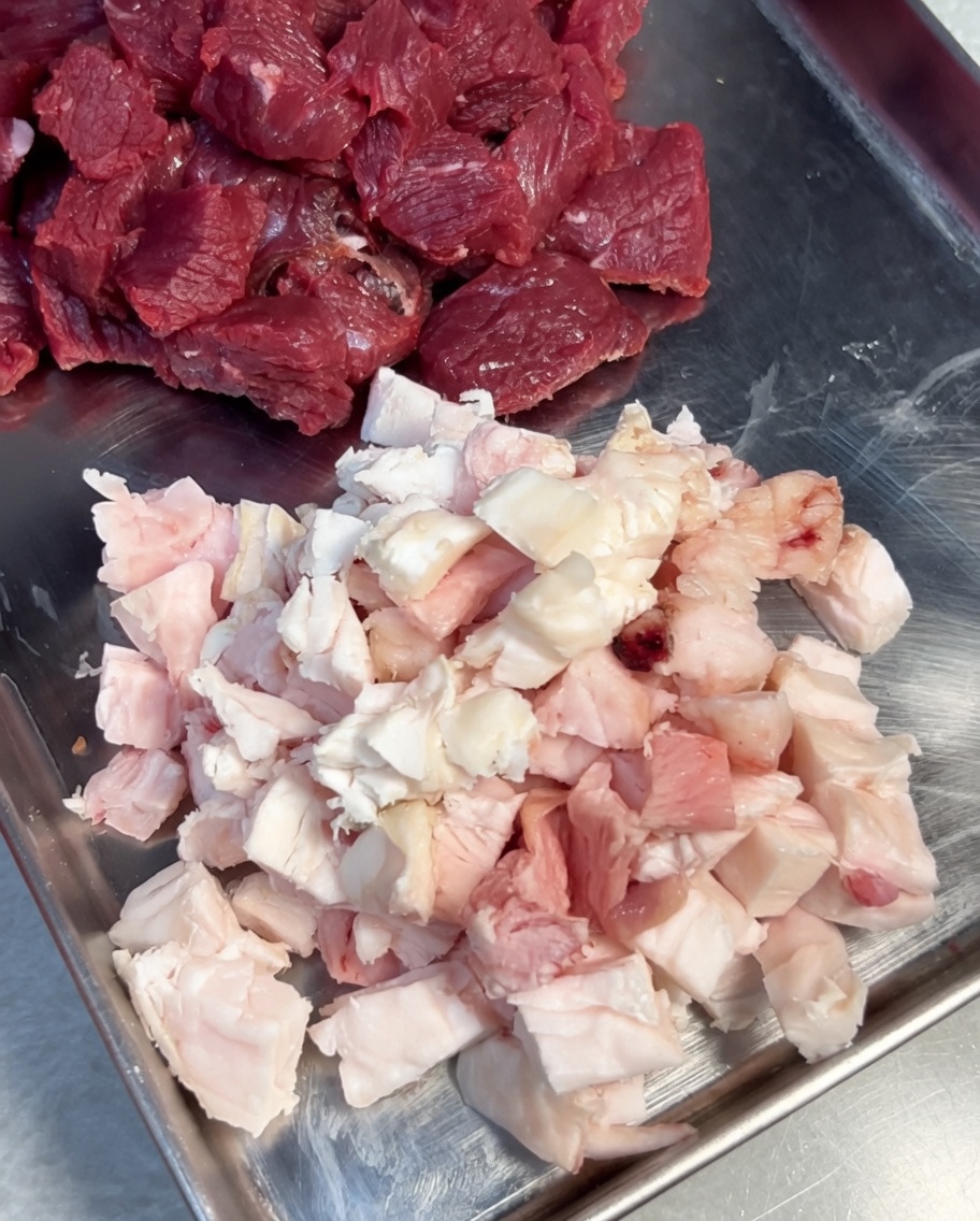 Rindfleisch und Fettstücke, die in einer Edelstahlschüssel mit Salz und schwarzem Pfeffer gewürzt werden.