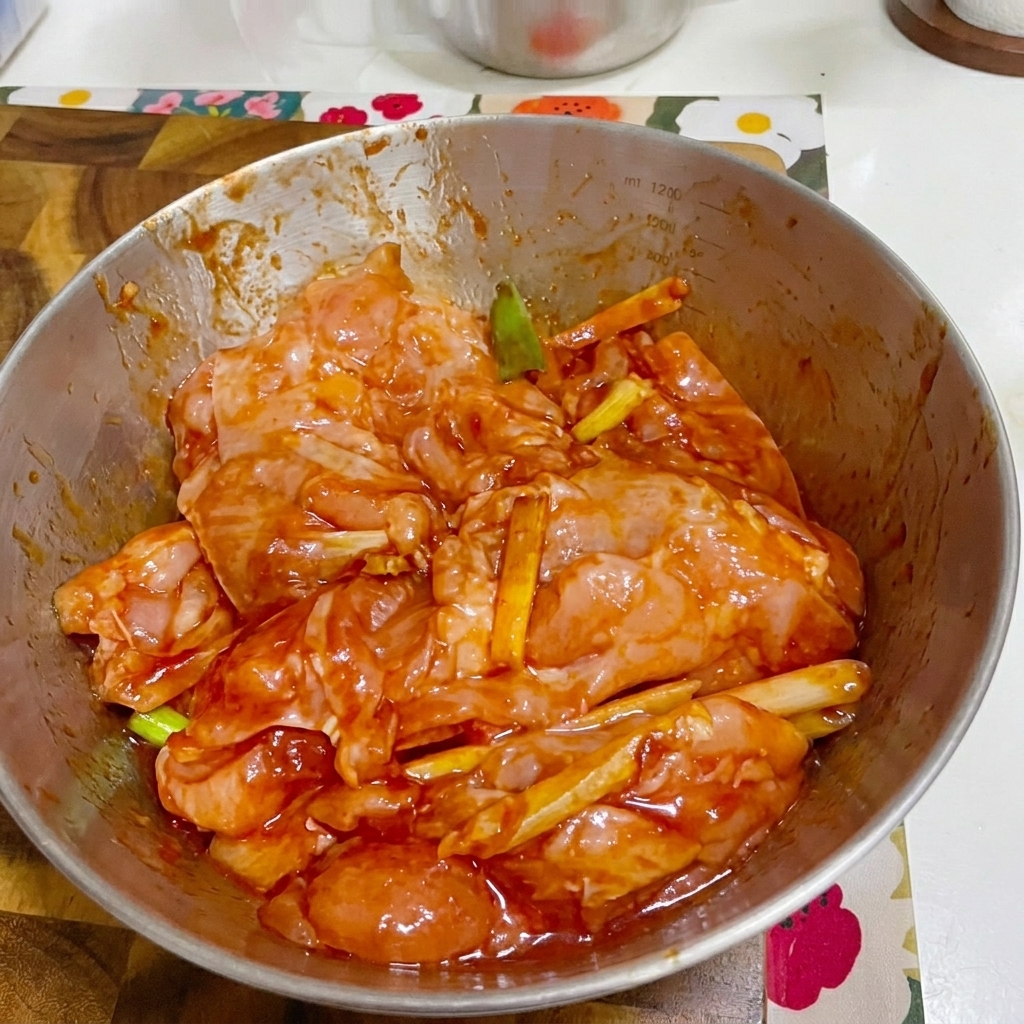 Eine Metallschüssel mit mariniertem Hähnchen, abgedeckt mit Frischhaltefolie.