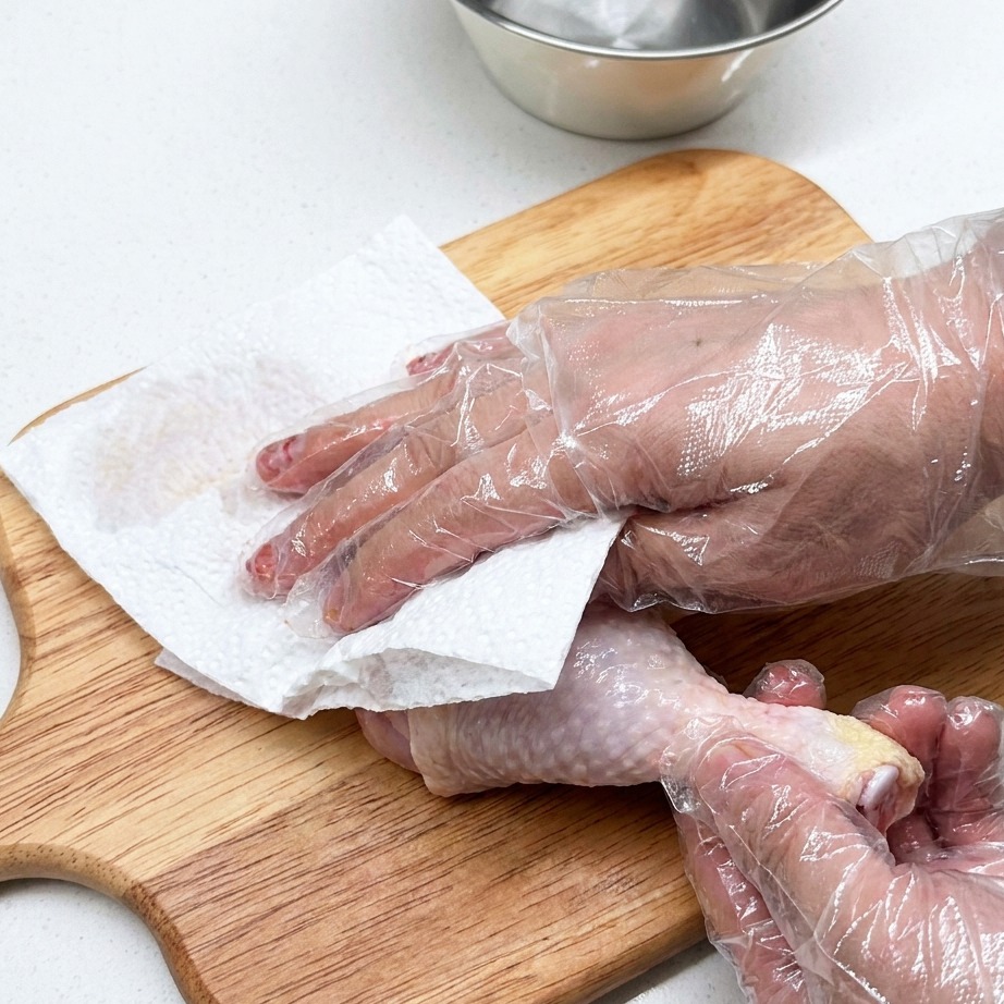 Rohe Hähnchenkeule, die auf einem Holzschneidebrett mit Papiertüchern vorbereitet wird.