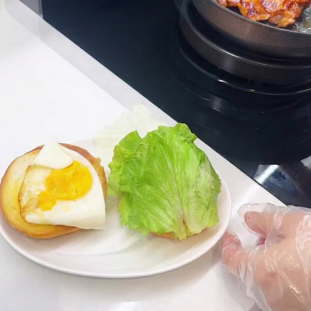 Eine Nahaufnahme vom Belegen des Burgers: Hähnchen, Käse, Ei und Salat werden auf dem Brötchen geschichtet.