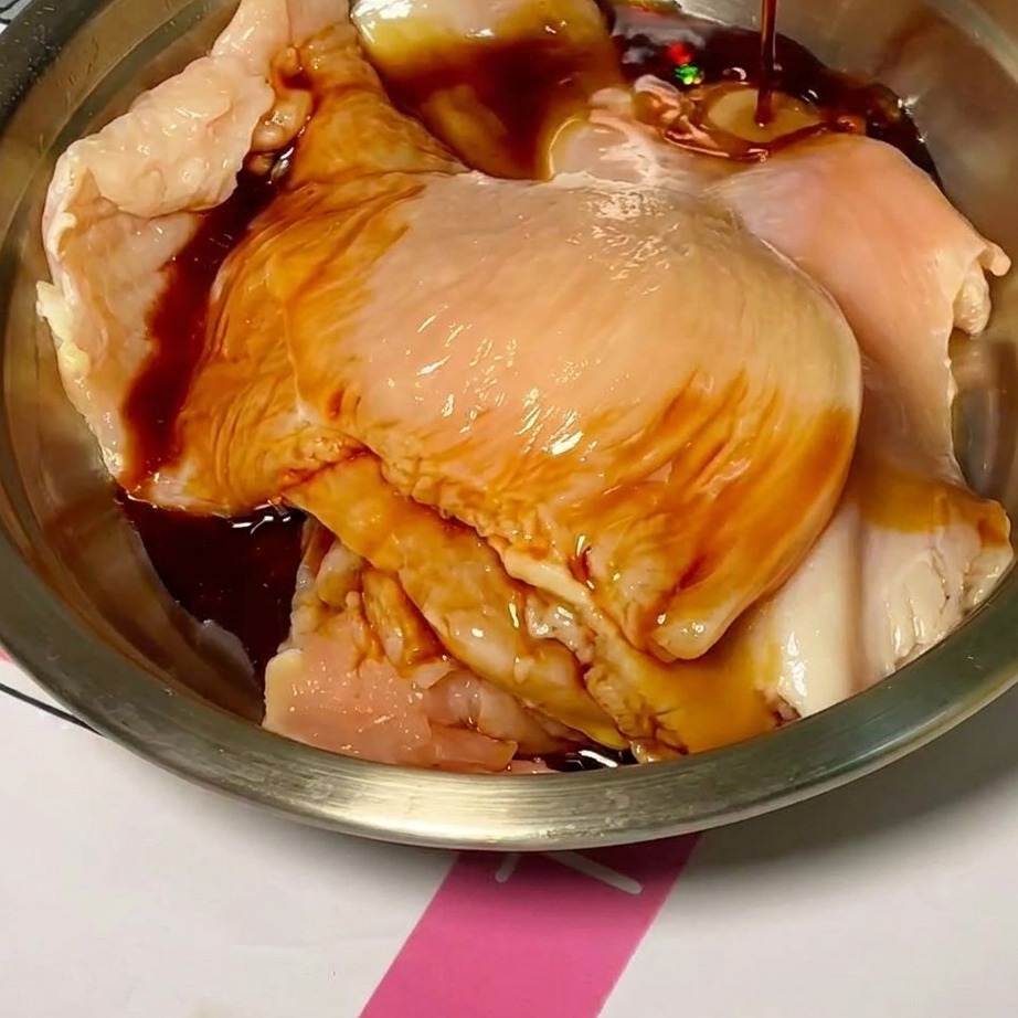 Rohe Hähnchenstücke in einer Rührschüssel, die mit einer dunklen, würzigen Marinade überzogen werden.