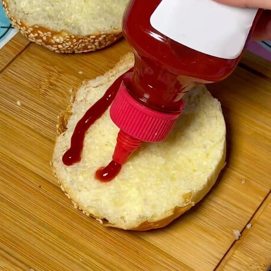 Ein Wirbel aus rotem Ketchup, der auf die Mitte eines getoasteten Sesambrötchens aufgetragen wird.