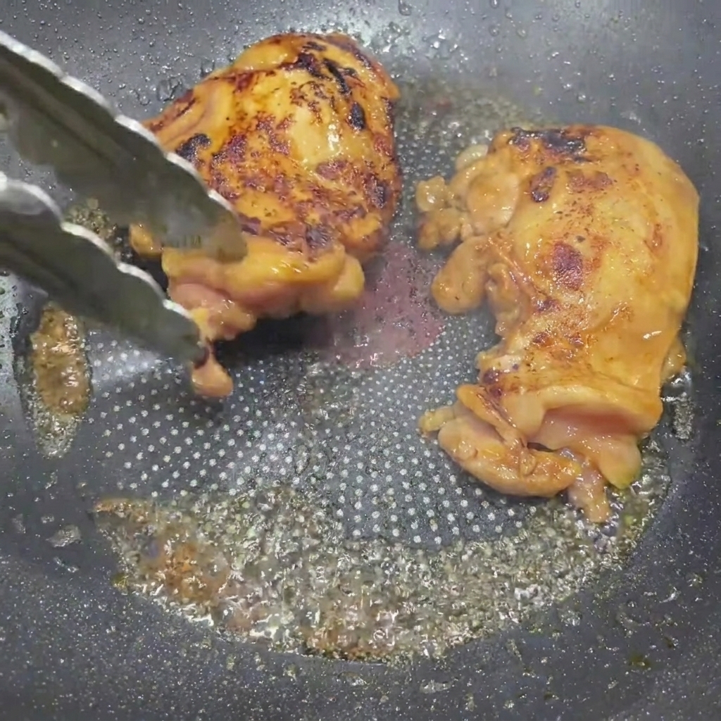 Goldbraun glasierte Teriyaki-Hähnchenschenkel werden in einer Bratpfanne mit einer Küchenzange gewendet.