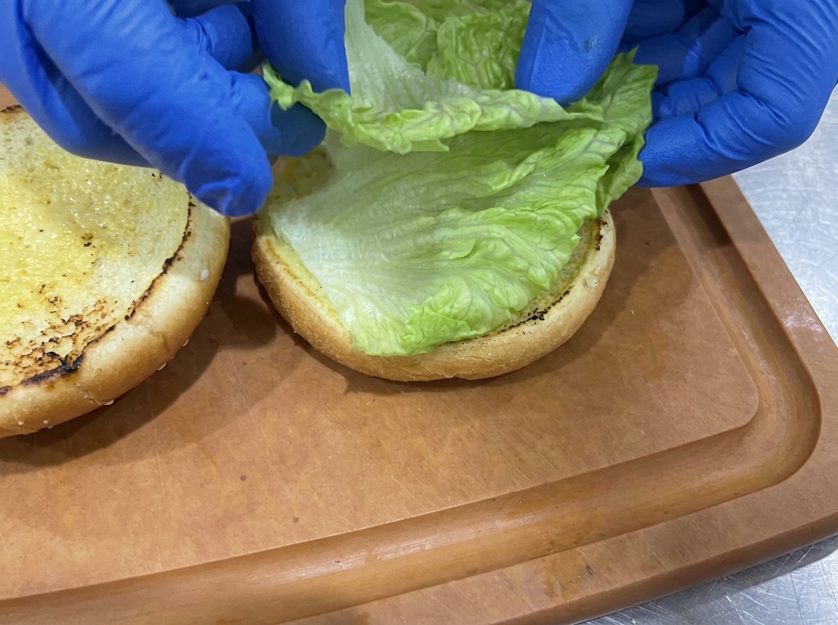 Knackig grüne Salatblätter werden auf der gerösteten unteren Hälfte eines Burger-Buns angerichtet.
