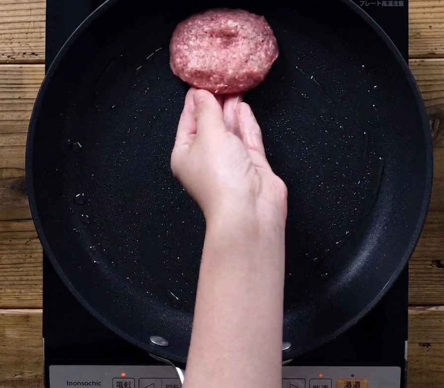 Ein Patty wird in eine leicht geölte Bratpfanne gelegt.