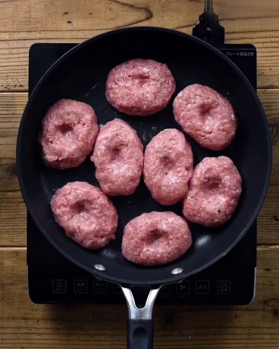 Patties in der Pfanne unter einem Glasdeckel.