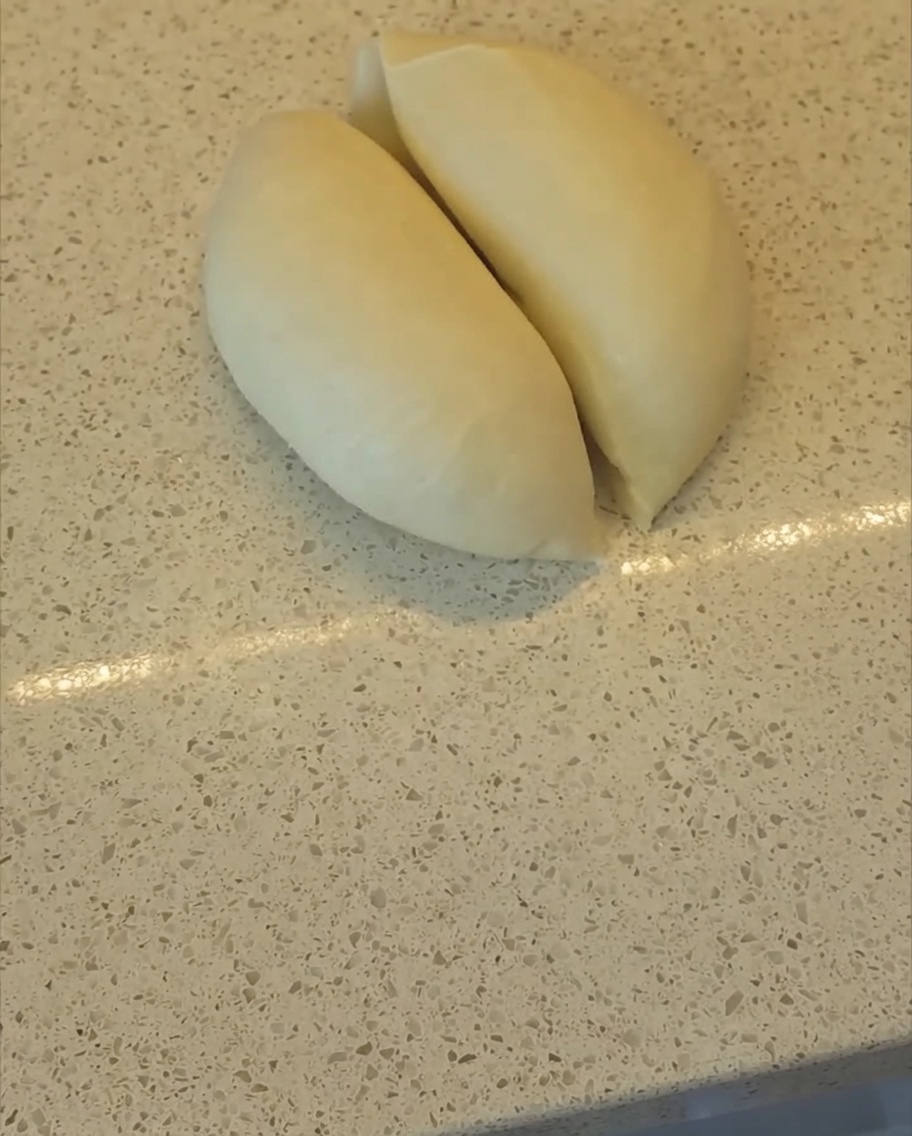 Eine Teigkarte teilt einen geschmeidigen Teigball in zwei gleiche Hälften auf der Arbeitsfläche.