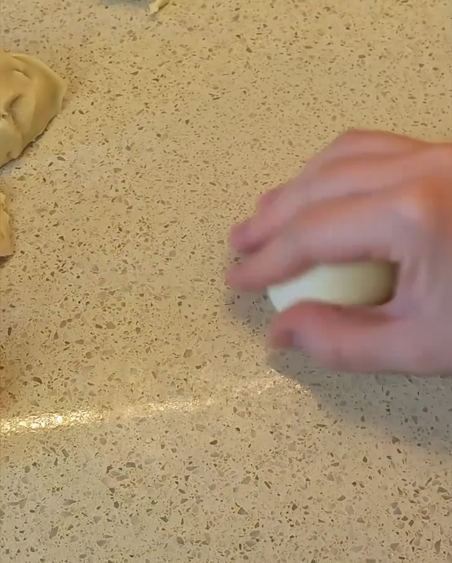 Eine Hand rollt ein Stück Teig auf der Arbeitsplatte zu einem glatten, runden Ball.