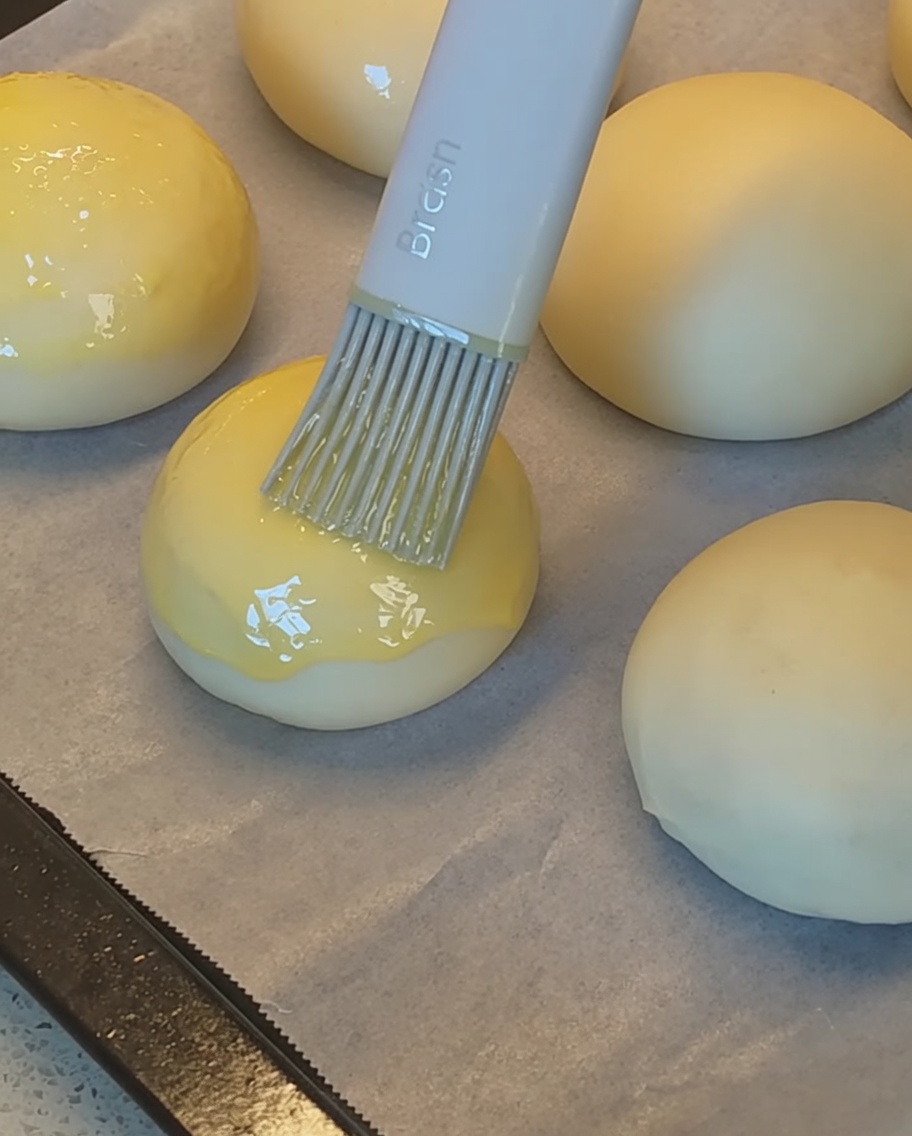 Ein Silikonpinsel bestreicht die Teiglinge mit Eistreiche vor der Bestreuung mit Sesam.