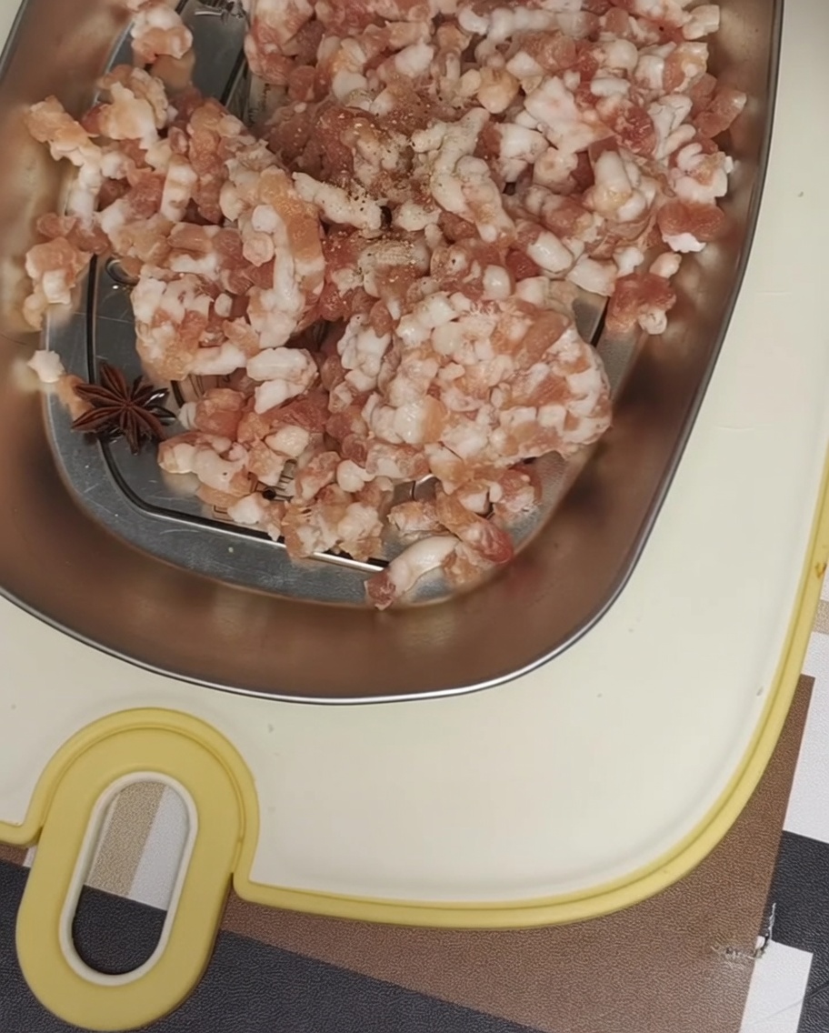 Schweinehackfleisch in einer Metallschale, gewürzt mit schwarzem Pfeffer und Meersalz.
