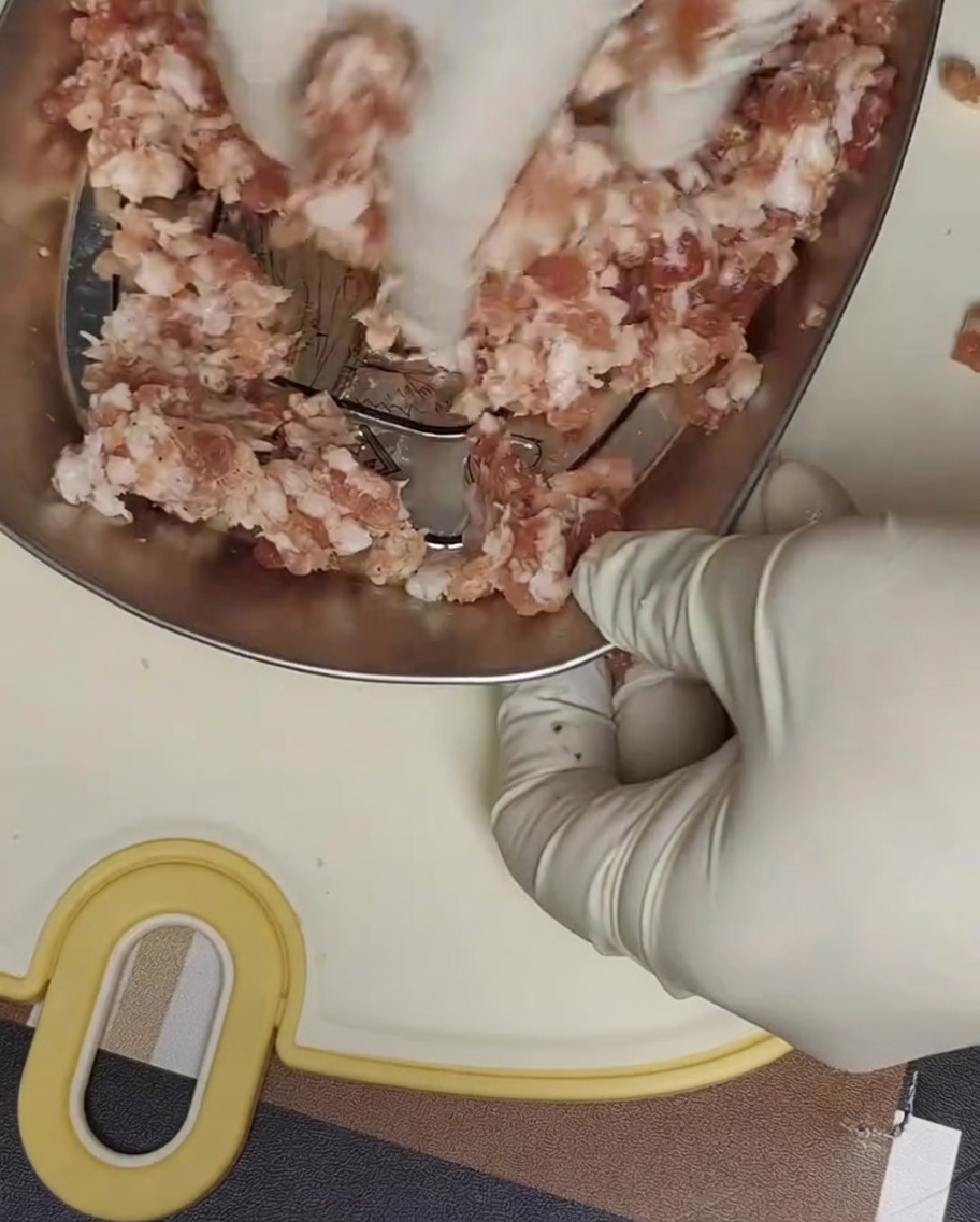 Behandschuhte Hände kneten gewürztes Schweinehackfleisch in einer Metallschale.