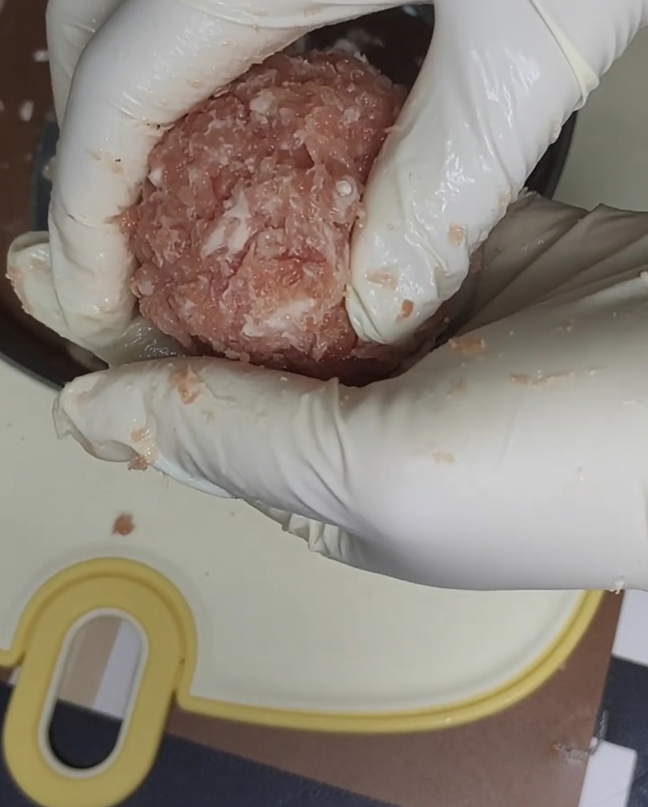 Schweinefleisch wird mit einer Metallform und Frischhaltefolie zu einem Patty geformt.