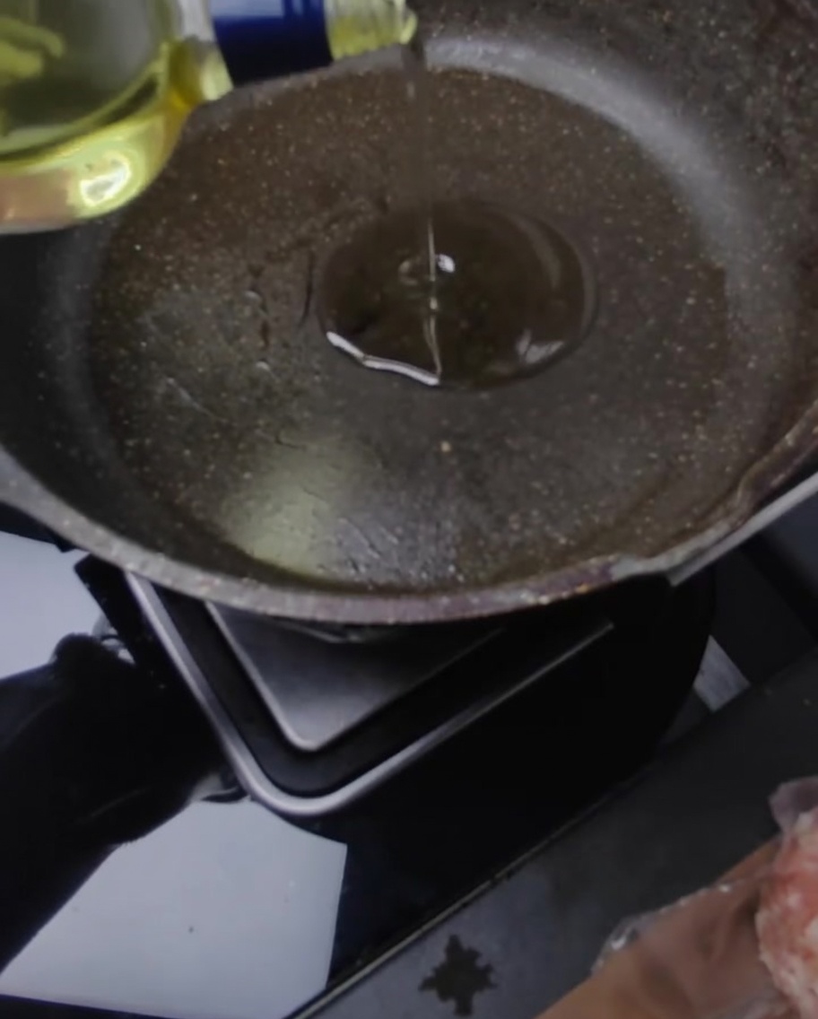 Ein Schweinefleisch-Patty brät in einer Pfanne mit Olivenöl und einem Stück schmelzender Butter.
