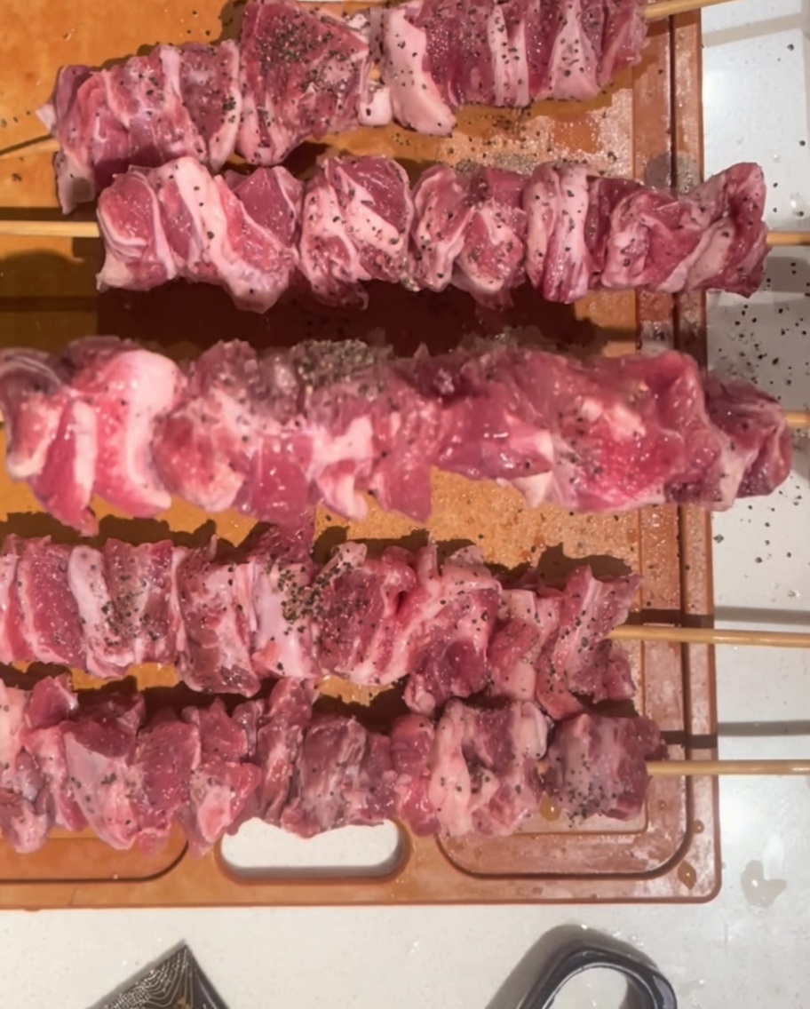 Die rohen, gewürzten Spieße werden auf dem Holzbrett gewendet, um die ungewürzten Seiten freizulegen.